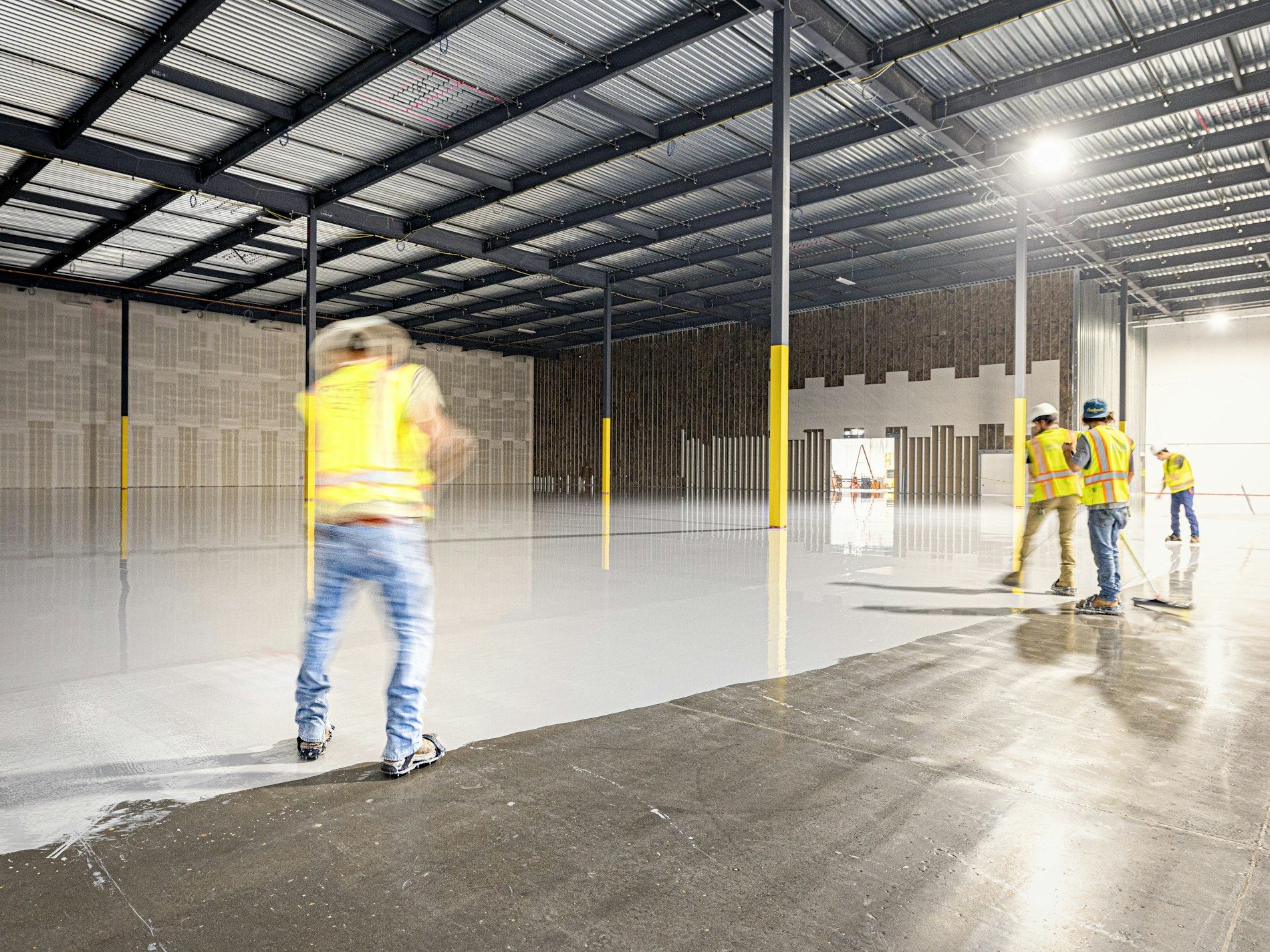 Workers in hi-vis apply resin coating across a warehouse floor