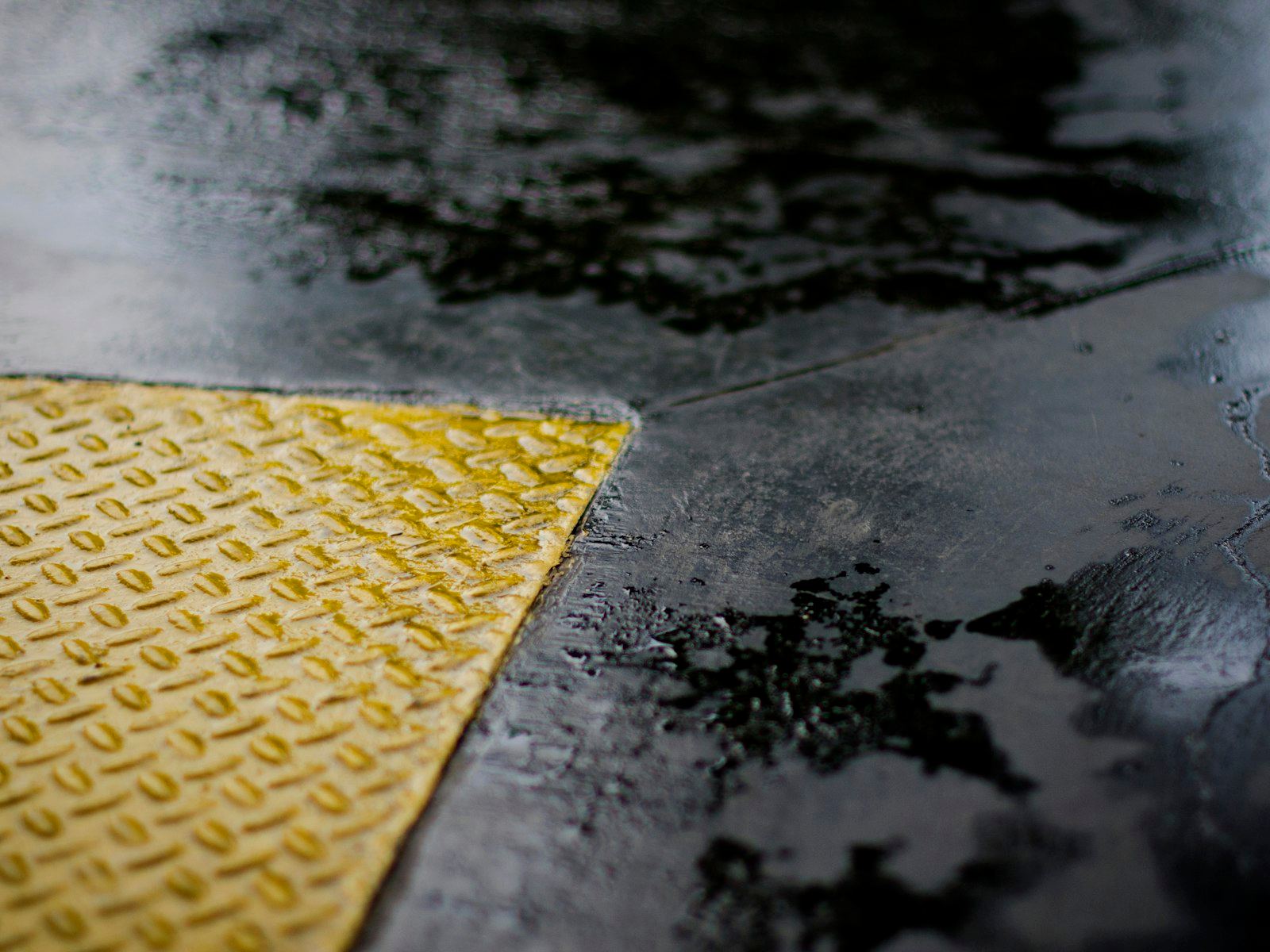 Close-up of a wet resin floor with a yellow diamond-plate safety edge.