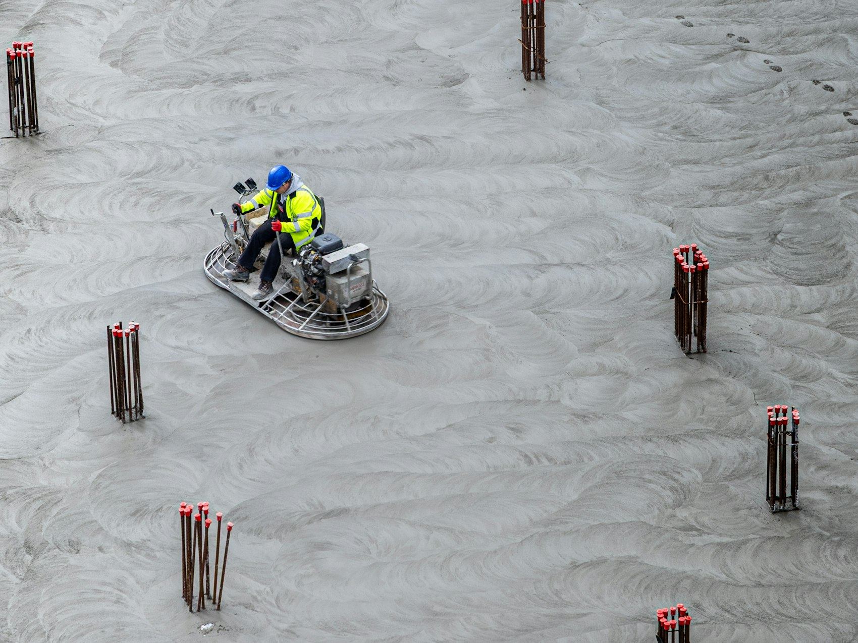 Worker using a power trowel to smooth a large wet concrete floor from above