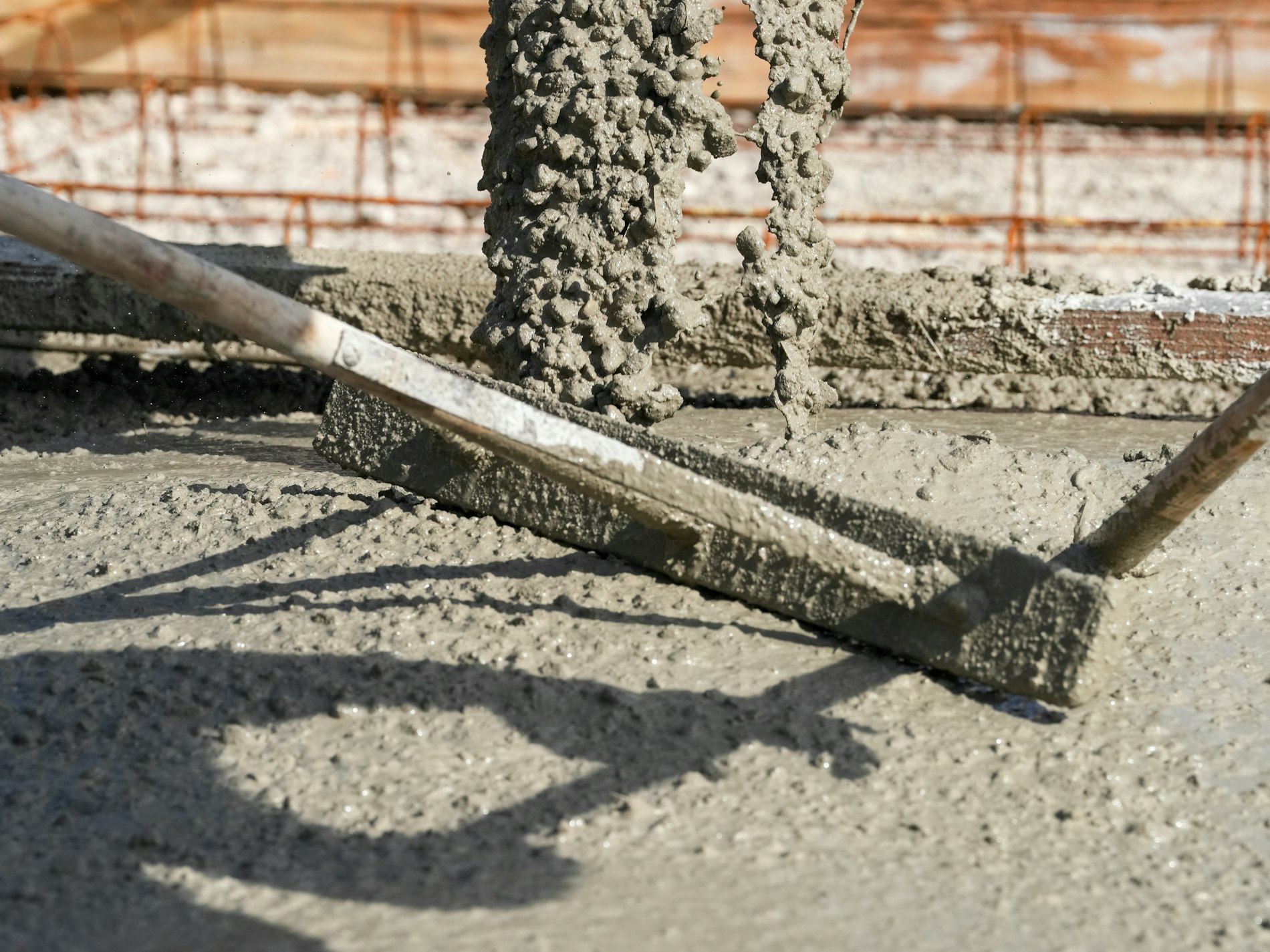 Two screed rakes resting on freshly poured concrete being leveled