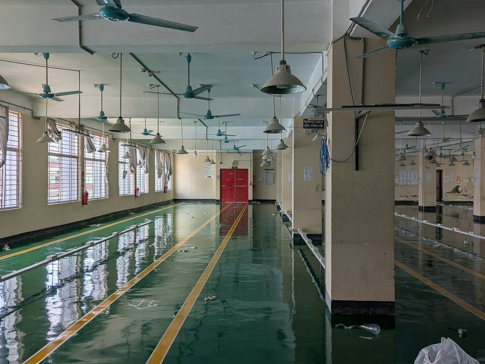 Empty hall with wet reflective floor and ceiling fans, red doors at the end.