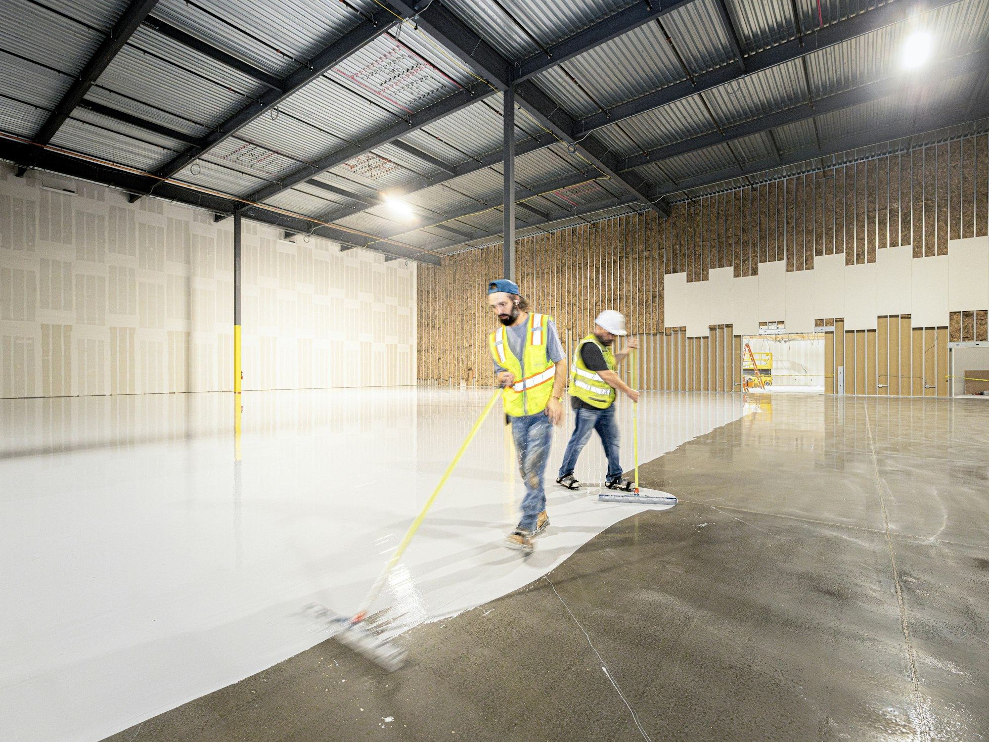 Two workers applying white resin coating to a warehouse floor