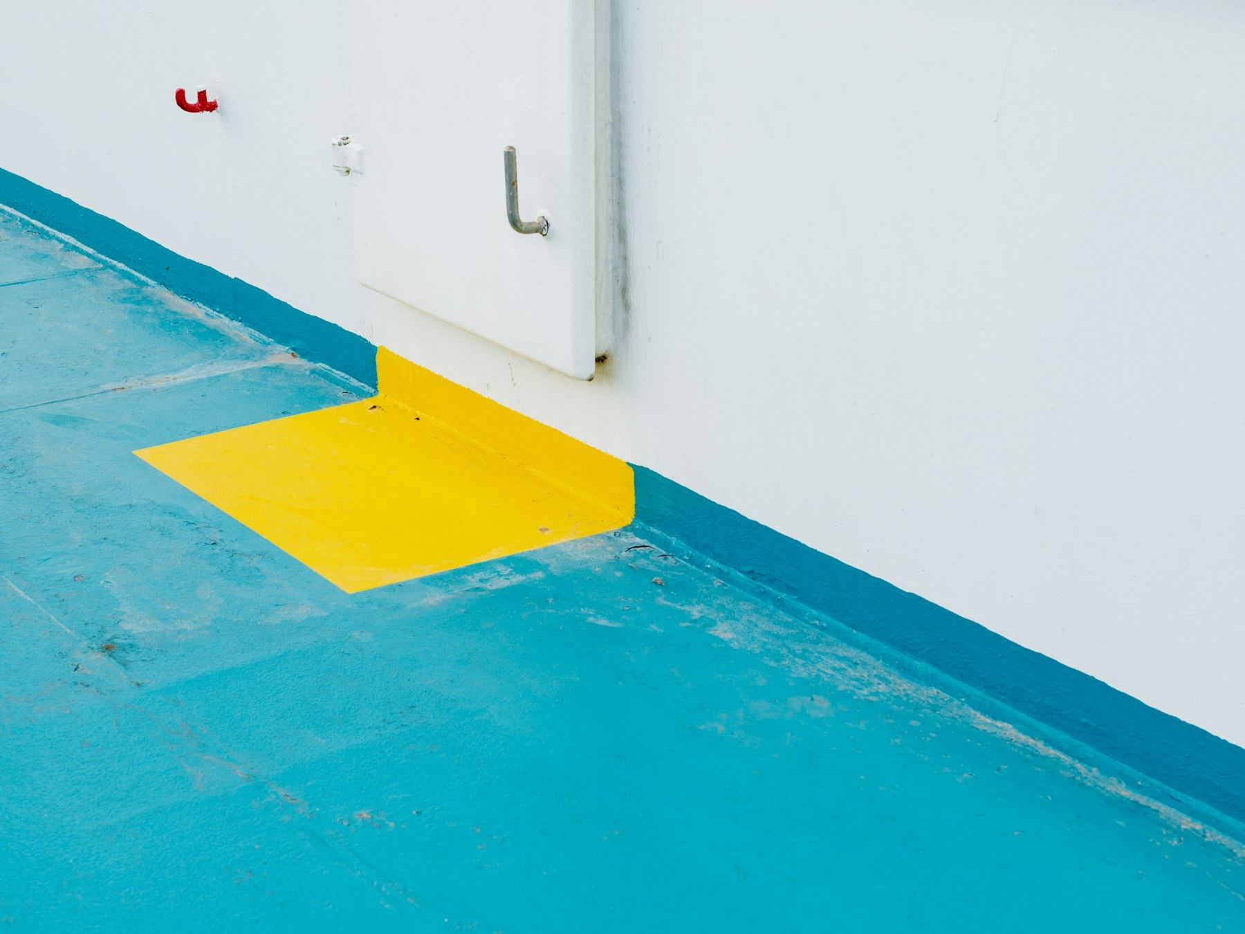 Close-up of a blue and yellow painted floor against a white wall.