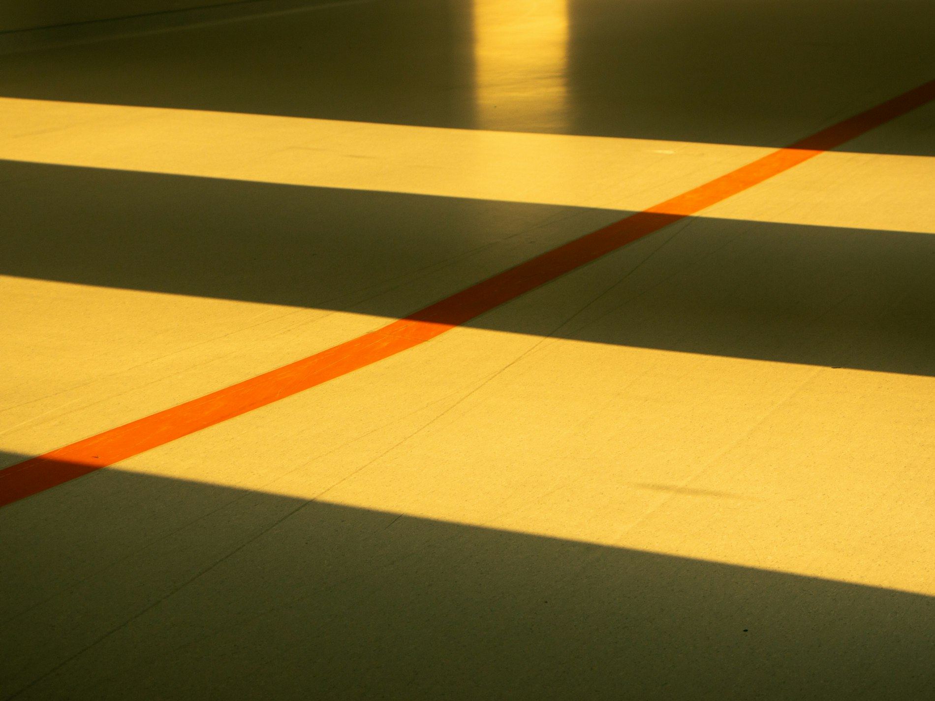 Close-up of sunlit gym floor with painted orange and yellow lines.