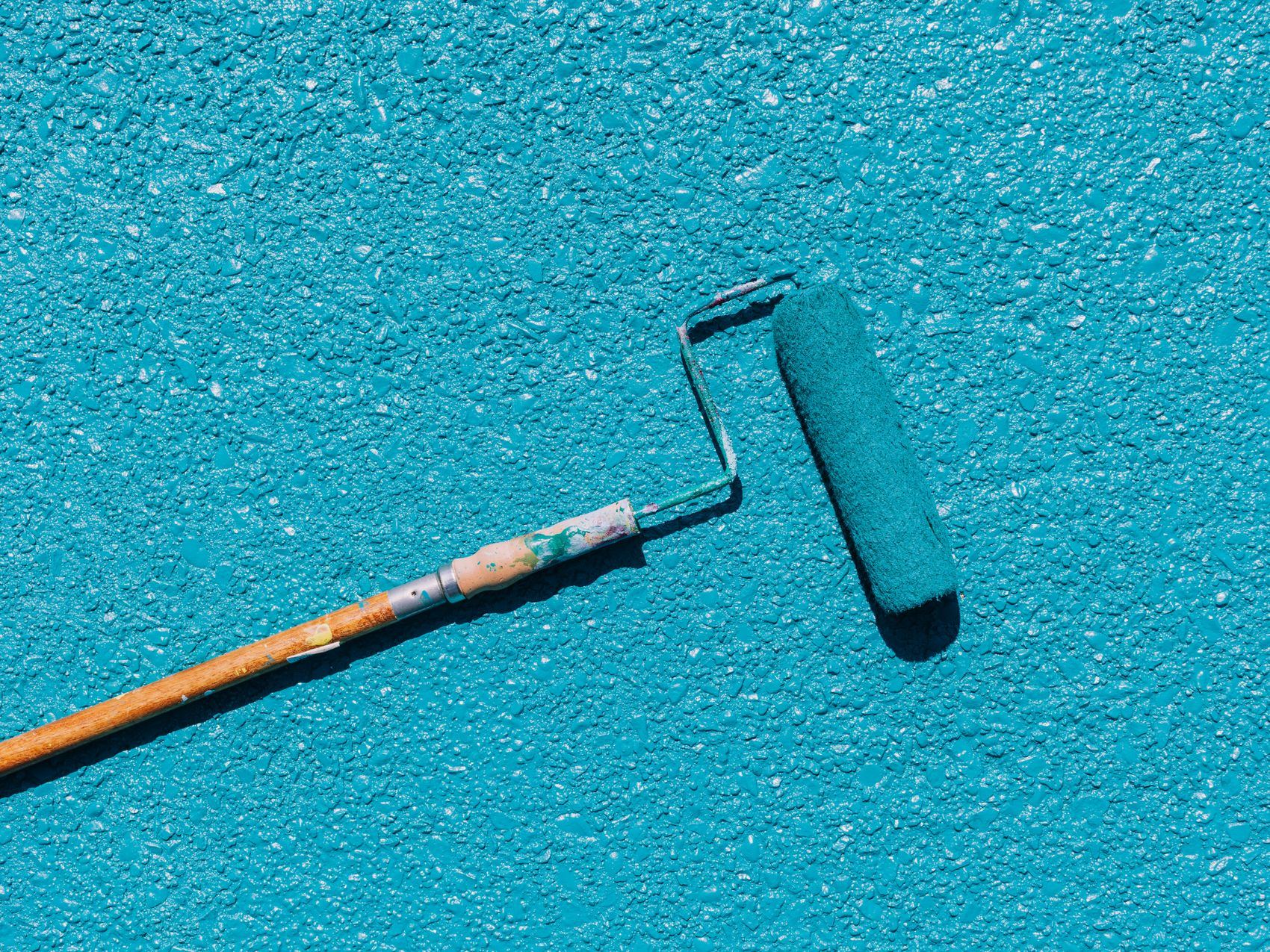 Close-up of a blue paint roller applying paint on a textured surface.
