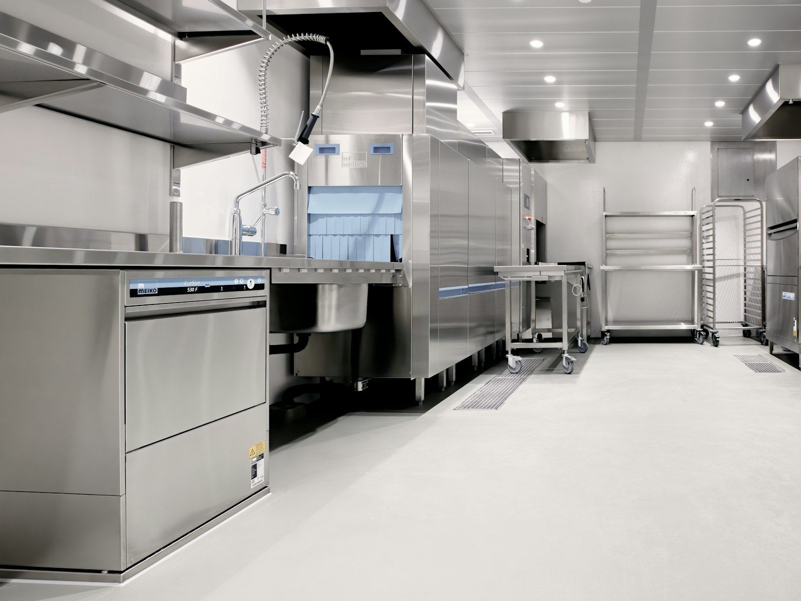 Commercial kitchen with stainless steel equipment and a pale resin floor.