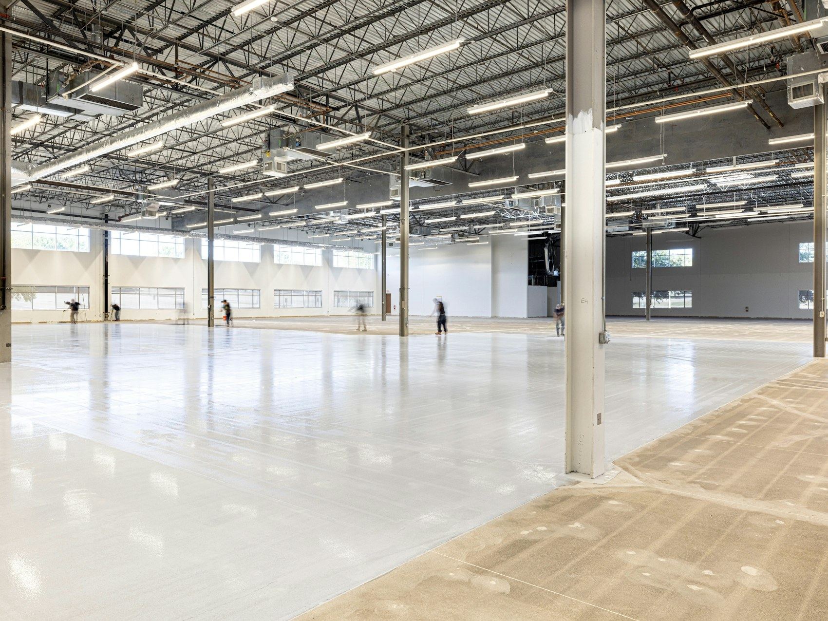 Large empty warehouse with a light-colored resin floor and overhead lighting.