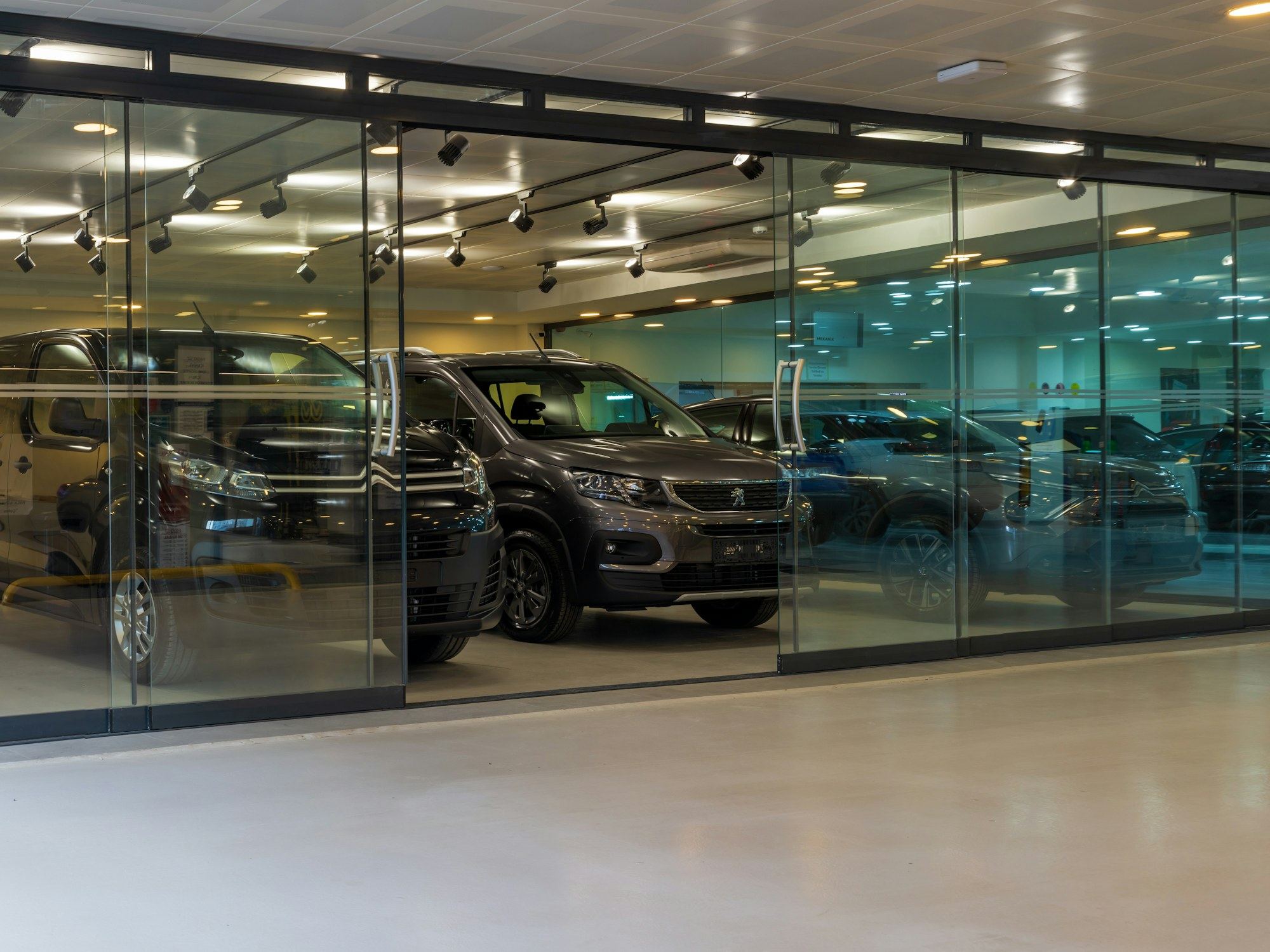 Several vehicles parked inside a bright glazed showroom with a light polished floor.